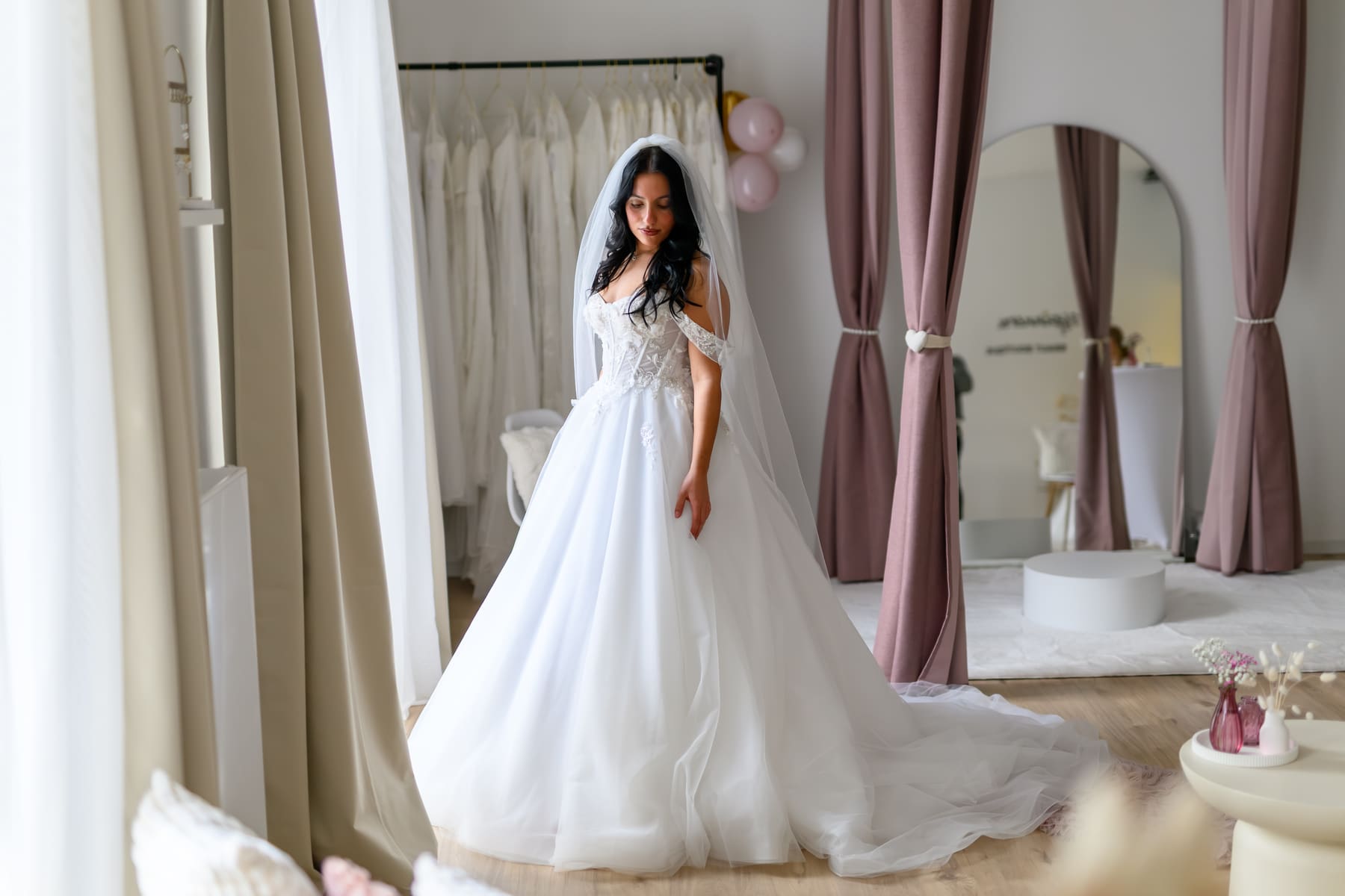 Braut in einem weiten Tüllkleid mit Schleier vor den Kleiderstangen der Herzspinnerei