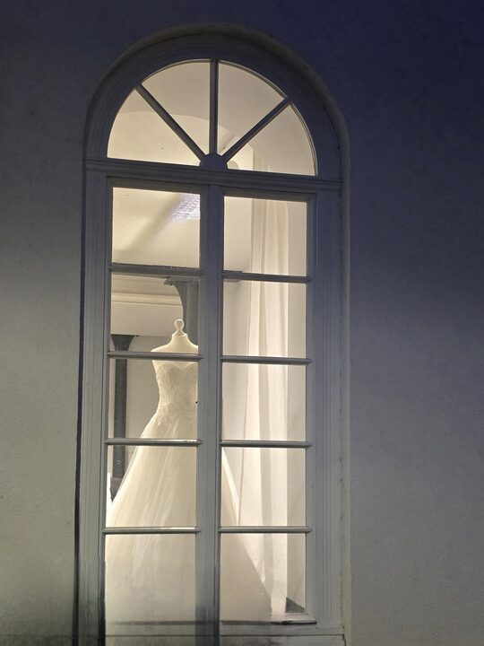 Beleuchtetes Rundbogenfenster der Herzspinnerei bei Nacht, dahinter ein Brautkleid