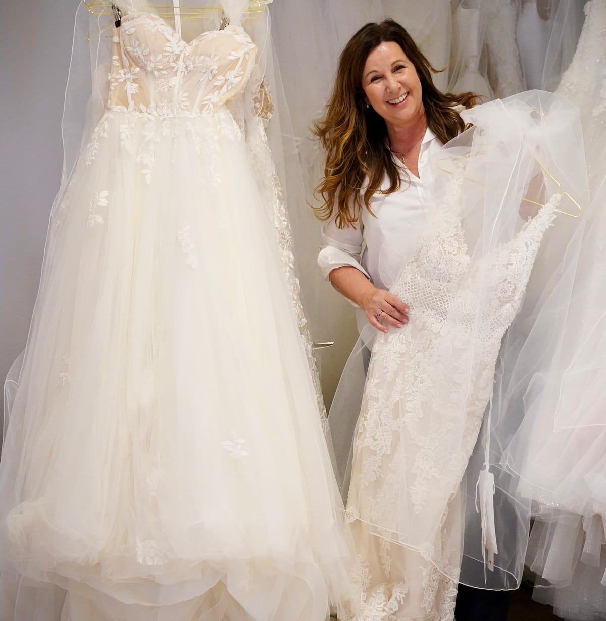 Ulrike Pausch zwischen zwei Brautkleidern an der Kleiderstange der Boutique