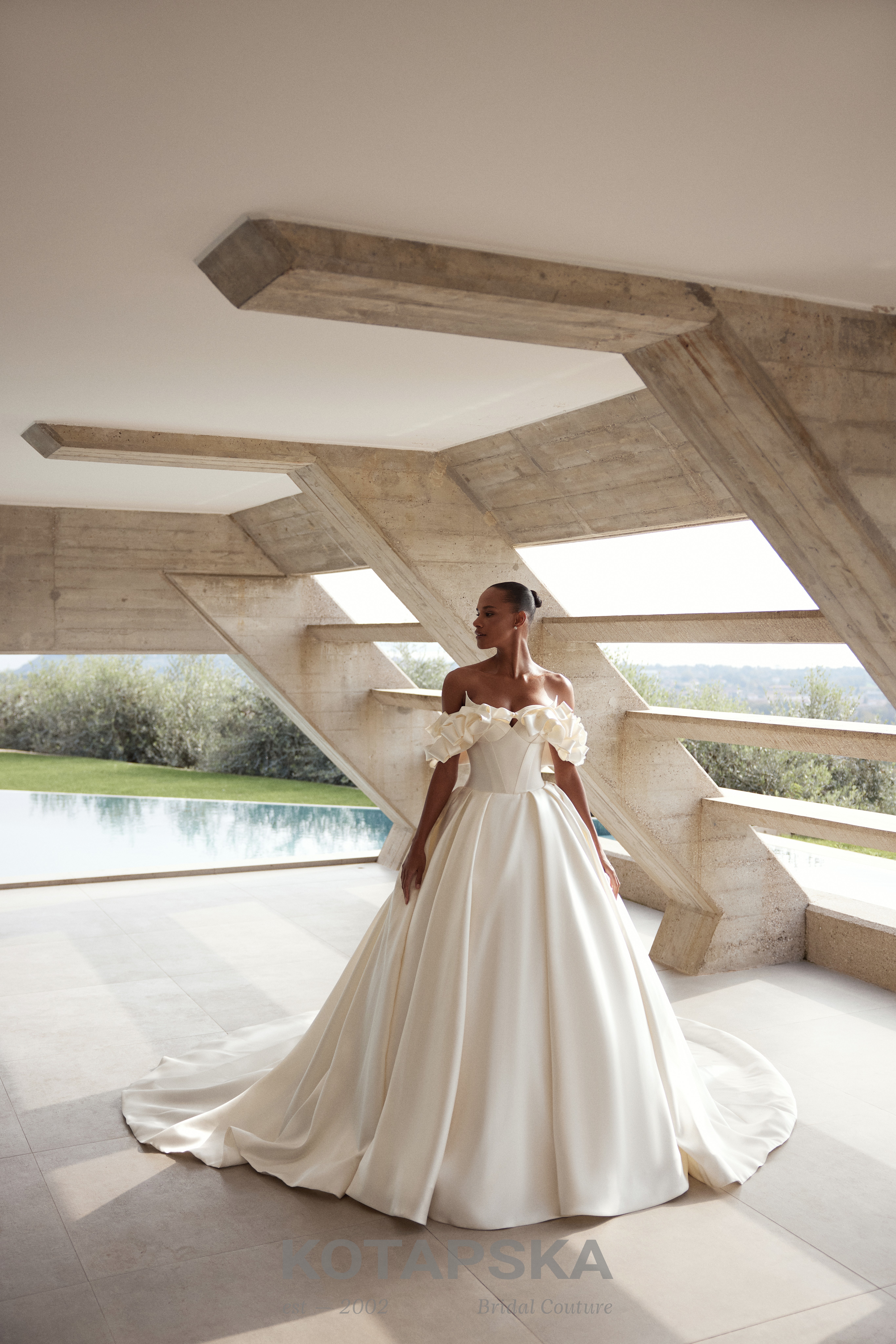 Dein Herzenskleid wartet — liebevoll präsentiertes Spitzenbrautkleid auf Mannequin vor hohem Bogenfenster, V-Ausschnitt und voluminösem Rock; Tischdekoration und gemütliches Sofa in der Herzspinnerei BRAUT BOUTIQUE Ettlingen.