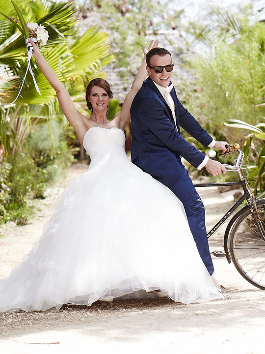 Brautpaar auf dem Fahrrad, die Braut im Tüllkleid mit Brautstrauß